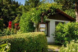 Ein traditionelles Gebäude mit Holzdach, umgeben von üppiger Vegetation und einer Statue.
