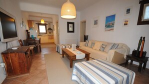 A living room with a sofa, a coffee table, and a TV. There is a kitchen in the background. - Divers House (Mykonos)