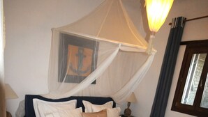 A bedroom with a bed, a canopy, a nightstand, a lamp, and a window. - Divers House (Mykonos)