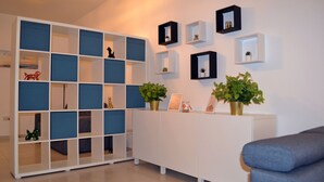 Ein modernes Wohnzimmer mit einem weißen Sofa, einer blau-weißen Schrankwand und einem weißen Konsolentisch mit Pflanzen und gerahmten Bildern.