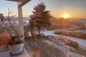 A snowy landscape with a large evergreen tree and a potted plant on a balcony.