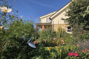 A house with a balcony, surrounded by a garden with various plants and flowers.