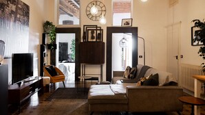 A living room with a sofa, a TV, a coffee table, and a plant. There is a clock on the wall and a window with blinds. - Renaissance Residence In San Miniato with a view (San Miniato)