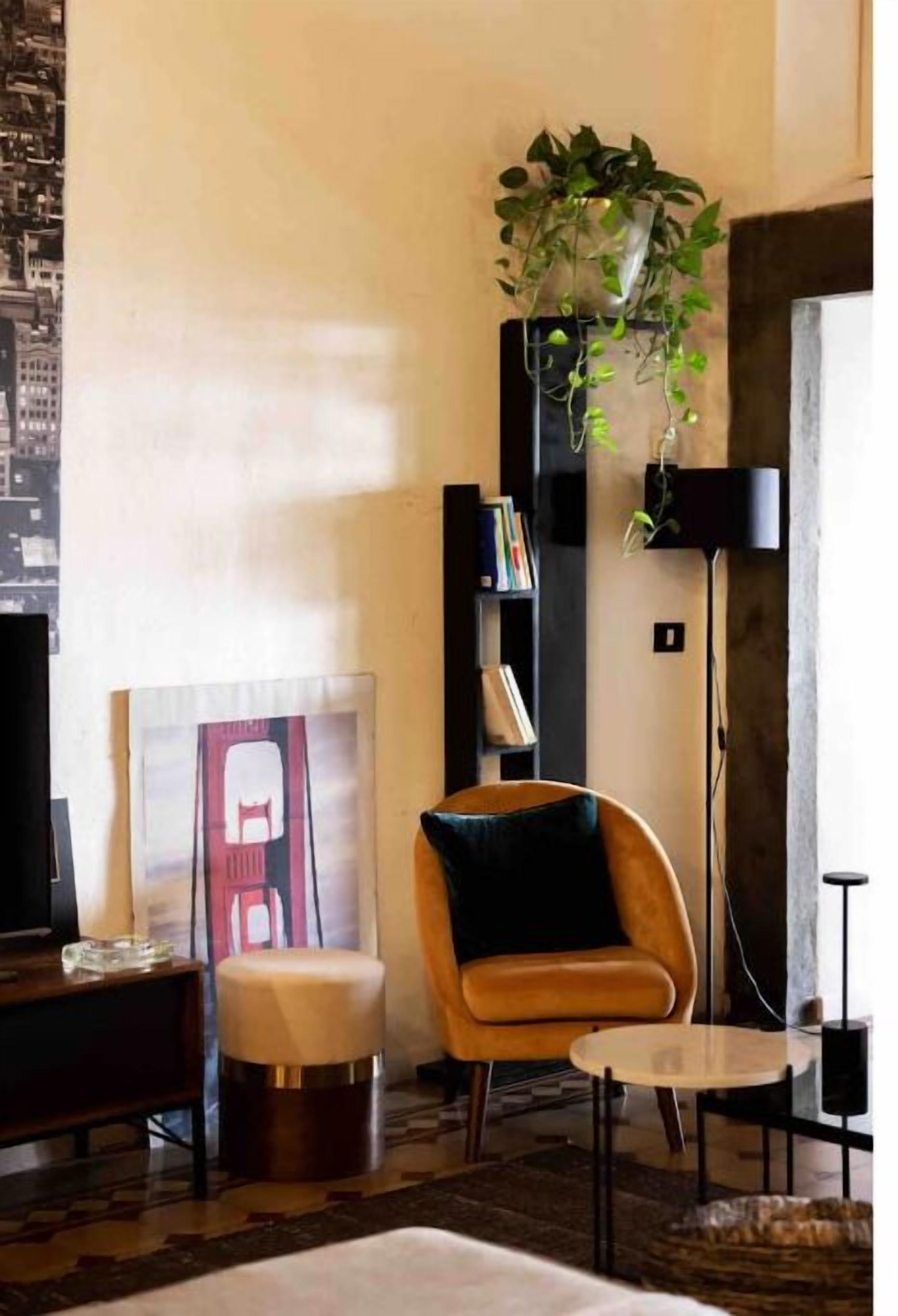 A modern living room with a sofa, ottoman, and a small table. There is a bookshelf and a hanging plant.