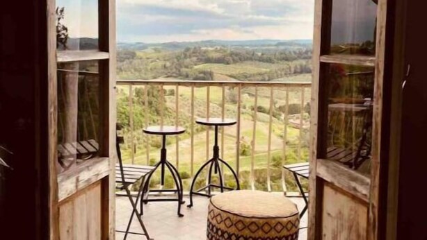A balcony with a view of a hilly landscape, a small round ottoman, and two tables. - Renaissance Residence In San Miniato with a view (San Miniato)