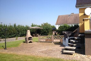 A backyard with a stone barbecue grill, a wooden fence, and a house with a tiled roof.