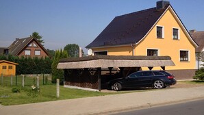 Uma casa amarela com telhado escuro, garagem coberta e quintal cercado.