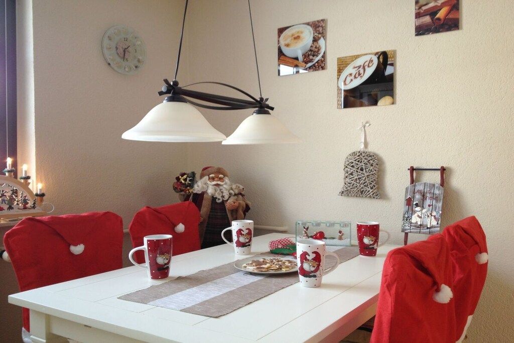 Un comedor con una mesa blanca, sillas rojas y decoraciones festivas.