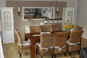 A dining area with a wooden table and wicker chairs, a white cabinet, and a mirror above the table. - Holiday home “Baltic Sea Dream” (Zudar)