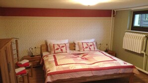 Quarto com cama de madeira, mesa de cabeceira, uma cadeira e radiador.