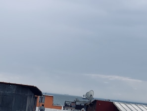Un toit surmonté d’antennes paraboliques, un navire à l’horizon et une vue sur la mer.