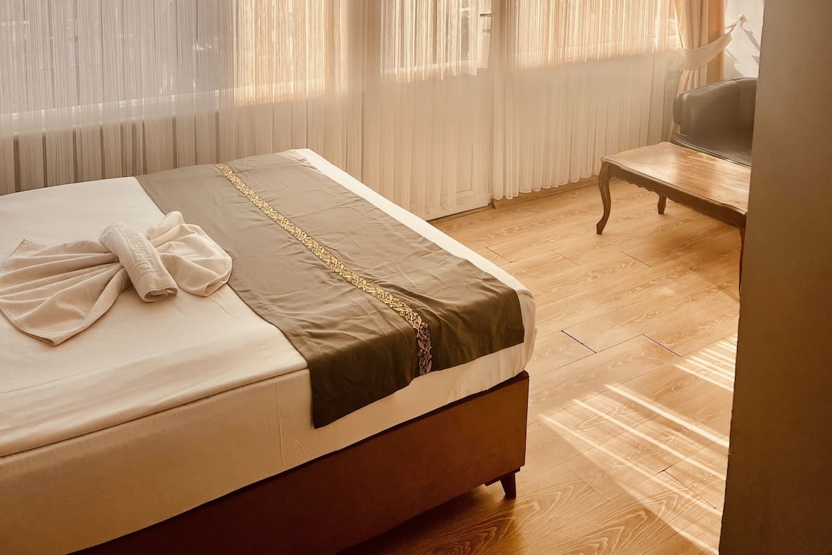 A hotel room with a bed, a chair, and sheer curtains.