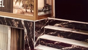 En hotellentrén med en marmortrappa, ett stort fönster med utsikt över palmer och en skylt med texten ”SAMI HOTEL”.