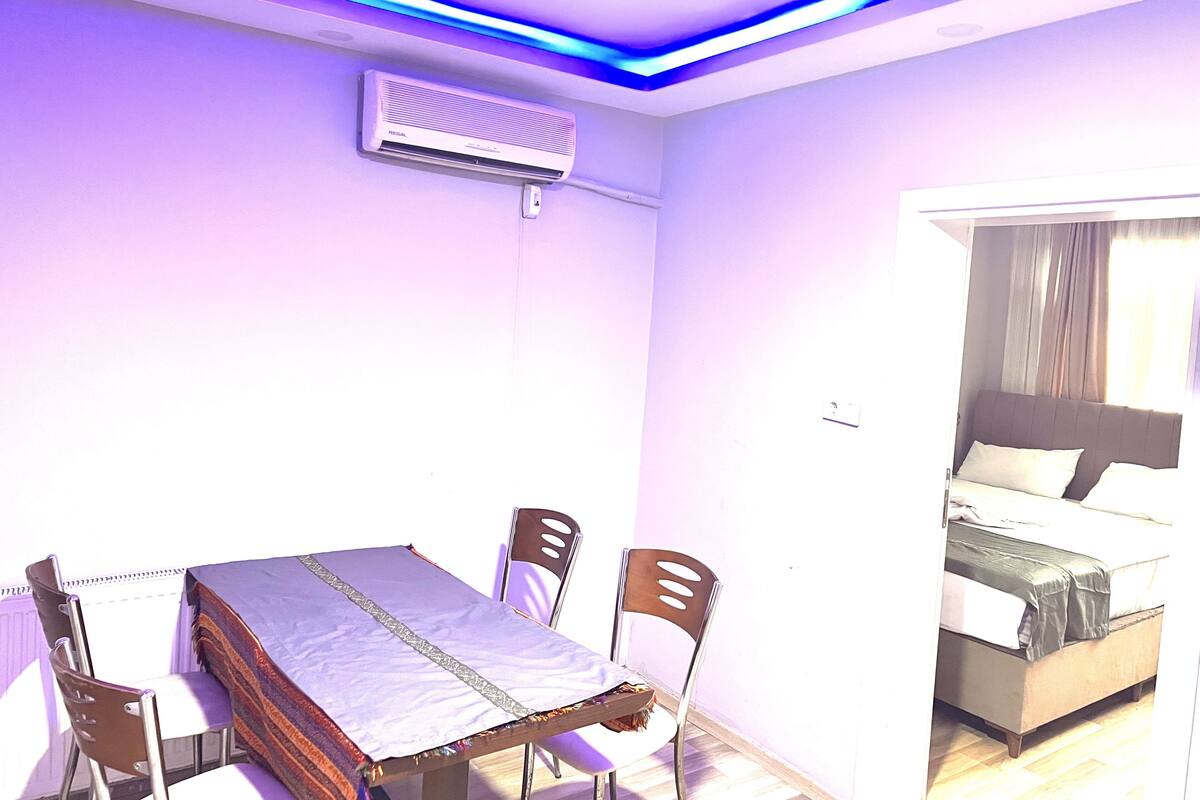 A room with a bed, a table, and chairs. There is an air conditioning unit on the wall.