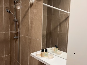 Une salle de bain avec une douche, un miroir et une étagère contenant des articles de toilette.