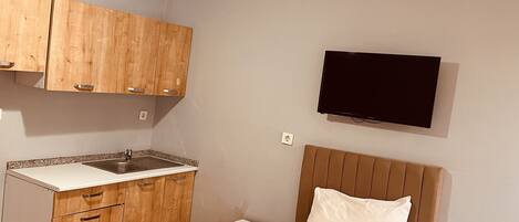 A compact room with a kitchenette, a bed, and a flat-screen TV.