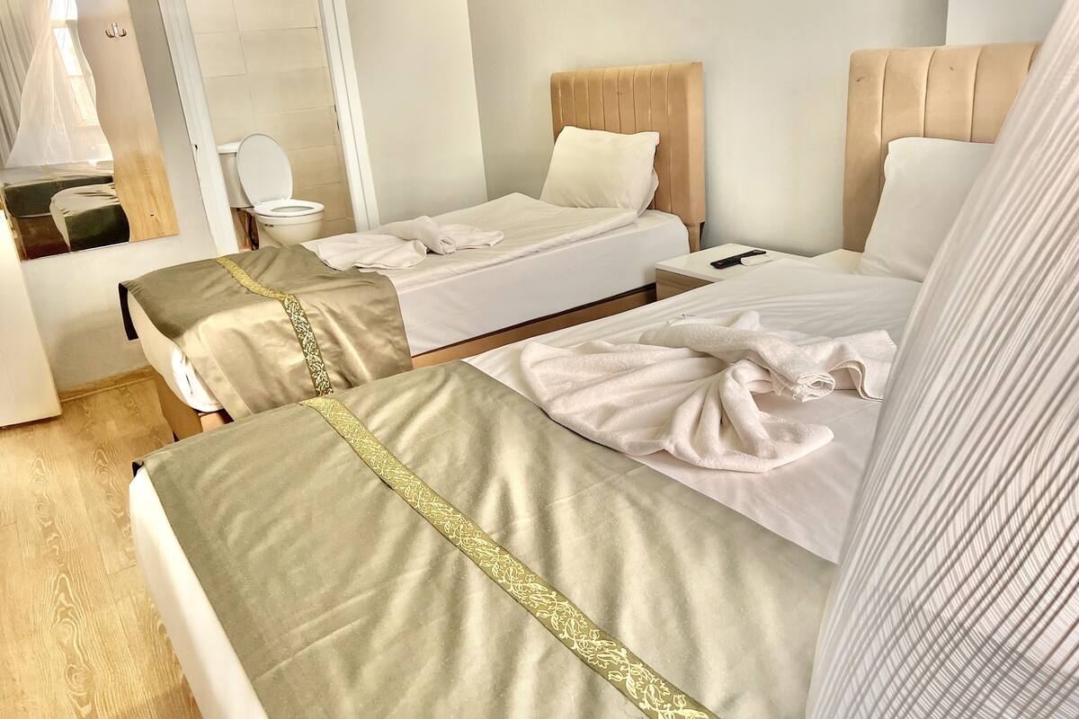A hotel room with two beds, a bedside table, a mirror, and a bathroom with a toilet and sink.