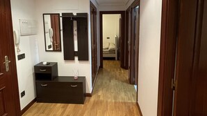 A hallway with wooden flooring, a mirror, a whiteboard, and a desk with drawers.