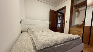 A bedroom with a bed, a wooden wardrobe, and a door leading to another room.