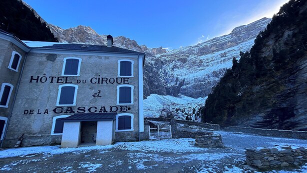 Kivestä rakennettu rakennus, jonka yläpuolella on kyltti, jossa lukee ”HOTEL DU CIRQUE et DE LA CASCADE”. Rakennuksessa on useita ikkunoita ja kivinen sisäänkäynti, ja se on lumihuippuisten vuorten ympäröimä.