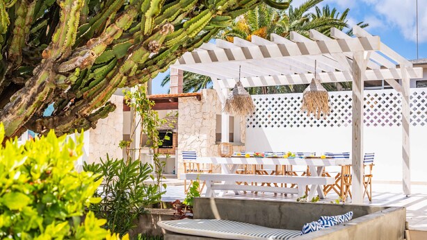 An outdoor patio with a white pergola, a dining table with blue and white striped cushions, and a hanging light fixture. - Casa do Cacto - By Wehost (Porto Santo)