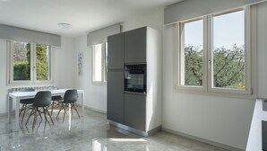 A modern kitchen with a dining area, large windows, and a view of greenery.