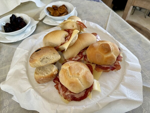 Une assiette de sandwichs au jambon et au fromage, accompagnée d’un bol de fruits secs et d’un bol de snacks frits.