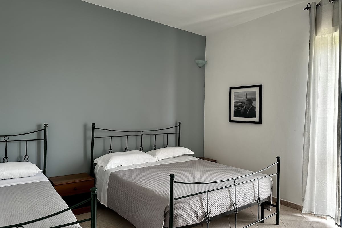 Een slaapkamer met twee eenpersoonsbedden, een nachtkastje, een lijst met een afbeelding aan de muur en een raam met gordijnen.