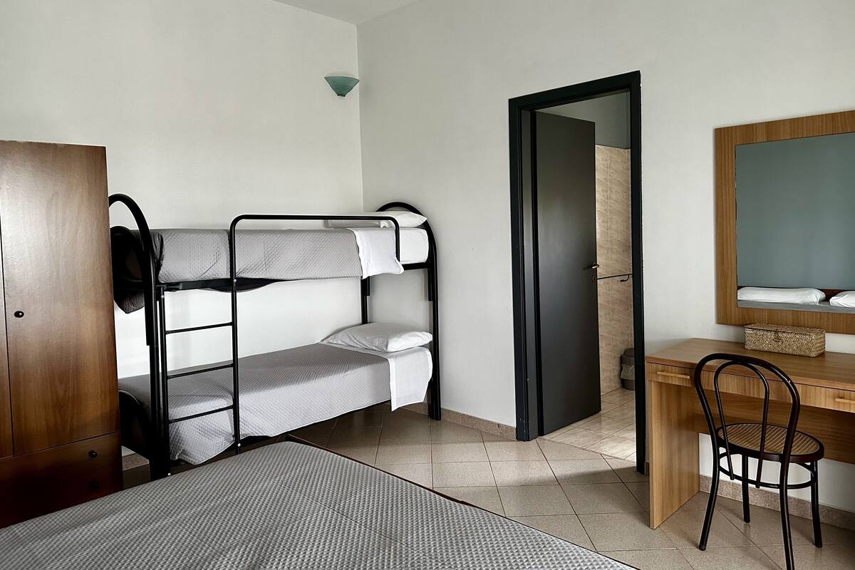Een kamer met een stapelbed, een bureau met stoel, een spiegel en een houten garderobe.