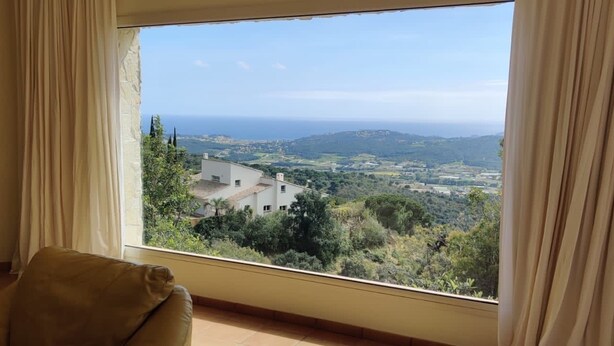Une pièce dotée d’une grande fenêtre donnant sur un paysage côtier, d’une cheminée et d’un canapé beige.