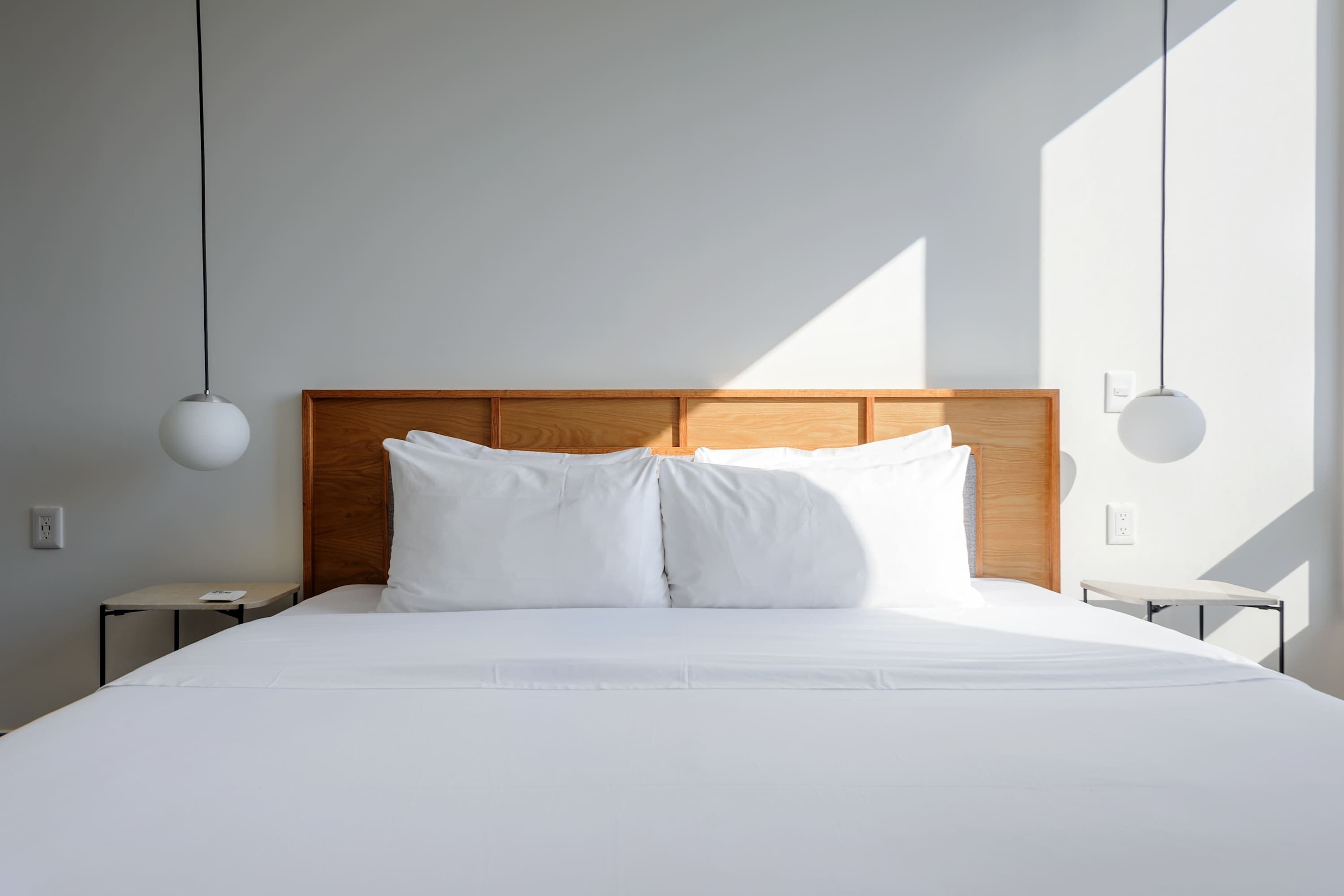 Un lit bien fait, avec du linge de lit blanc, une tête de lit en bois et deux tables de chevet avec des lampes.