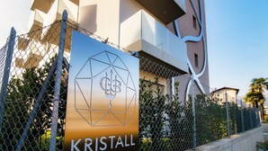 Ketjulinkkiaidassa on kyltti, jossa lukee ”KRISTALL”, ja taustalla näkyy modernilla arkkitehtuurilla suunniteltu rakennus.