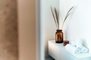 Ein Badezimmer mit einem weißen Waschtisch, einer braunen Vase mit Pampasgras und aufgerollten Handtüchern.