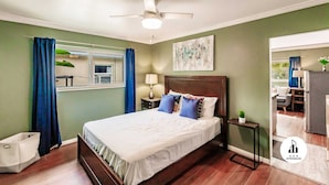 A bedroom with a bed, a ceiling fan, a nightstand, a lamp, and a window with curtains. - Uhost AI | Hollywood Garden 1BR Family Spot (Hollywood)