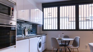Eine moderne Küche mit Einbauofen, Mikrowelle und Waschmaschine, ein Essbereich mit Tisch und Stühlen sowie ein Fenster mit Gitterverglasung.