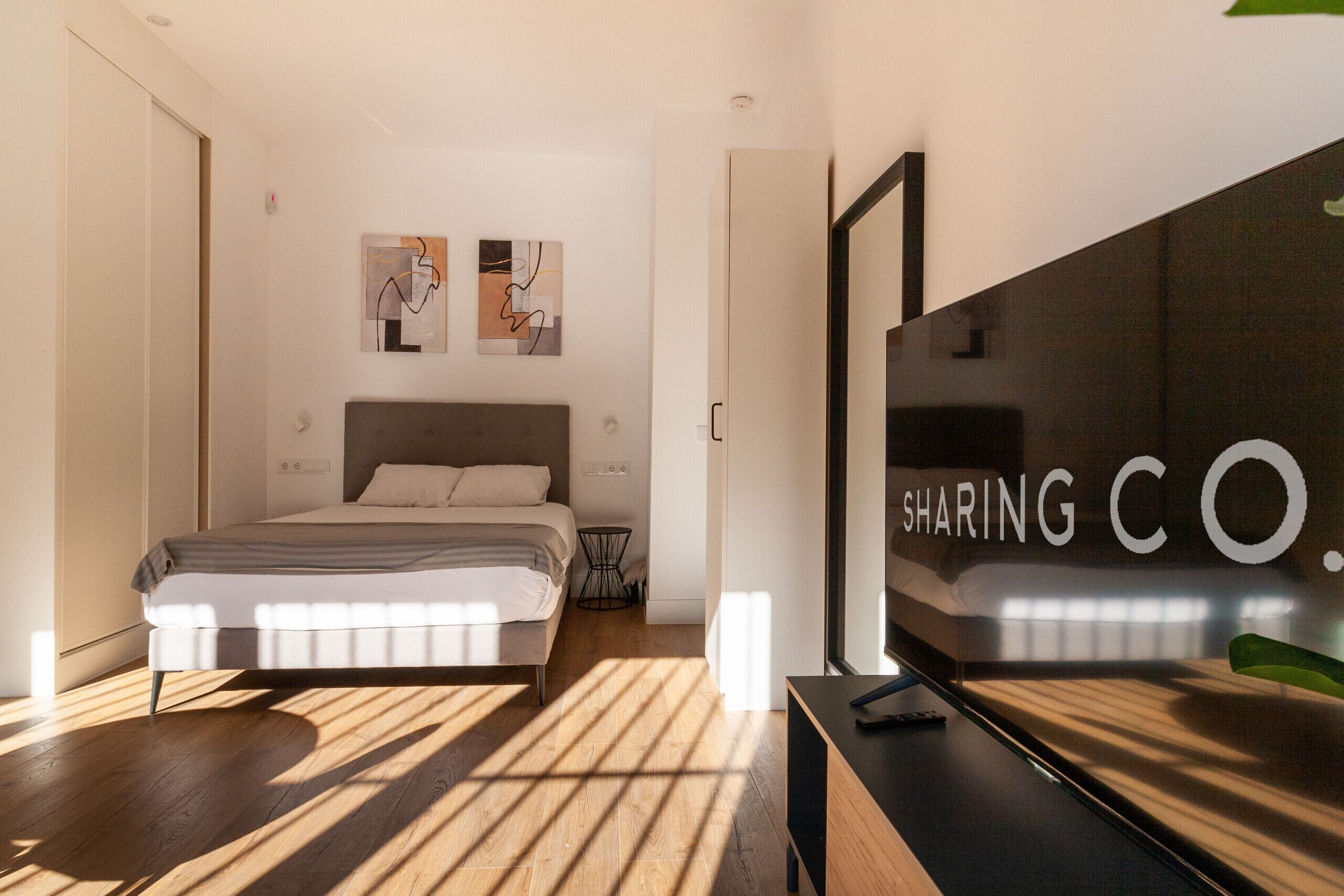 Un dormitorio moderno con cama, mesita de noche pequeña y televisor sobre un mueble.