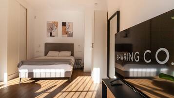Un dormitorio moderno con cama, mesita de noche pequeña y televisor sobre un mueble.