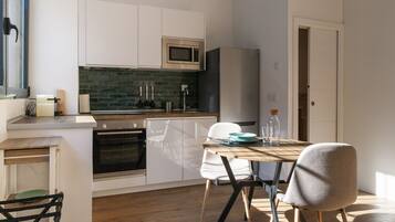 Una cocina moderna con armarios blancos, microondas, horno y un comedor con mesa y sillas.