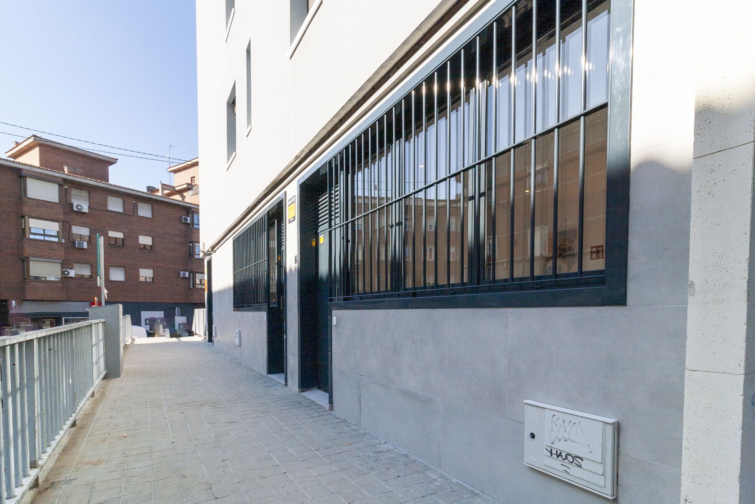 Un estrecho callejón urbano con un edificio que tiene ventanas amplias y una puerta de metal.