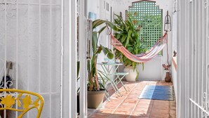 A narrow outdoor corridor with a tiled floor, a hammock, potted plants, and a small table with chairs.