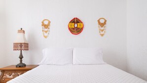 A neatly made bed with white bedding, a wooden nightstand with a lamp, and decorative wall hangings.