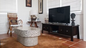 A living room with a round coffee table, a television on a dark wooden stand, a patterned rug, and a chair with a decorative cushion.