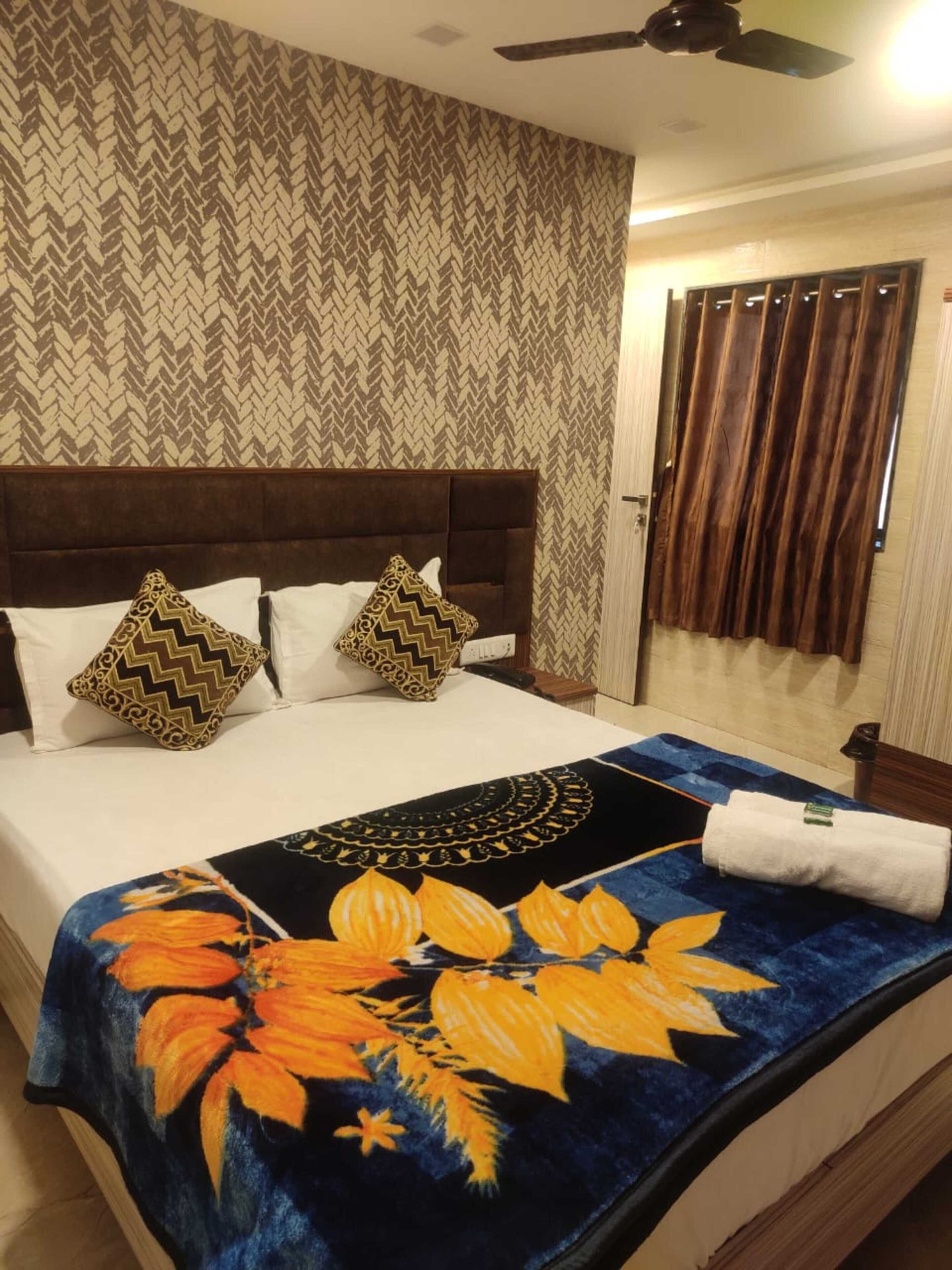 A neatly made bed with a floral bedspread, a brown upholstered headboard, and two patterned pillows.