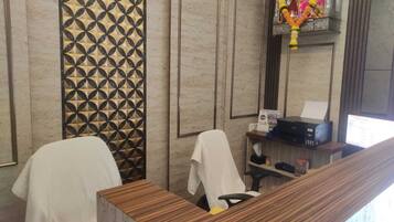 A reception area with a wooden reception desk, a patterned wall, and a small shrine with garlands.