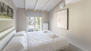 Ein Schlafzimmer mit einem Bett, einer weißen Klimaanlage, einem gerahmten Kunstwerk und Blick durch eine Glastür.
