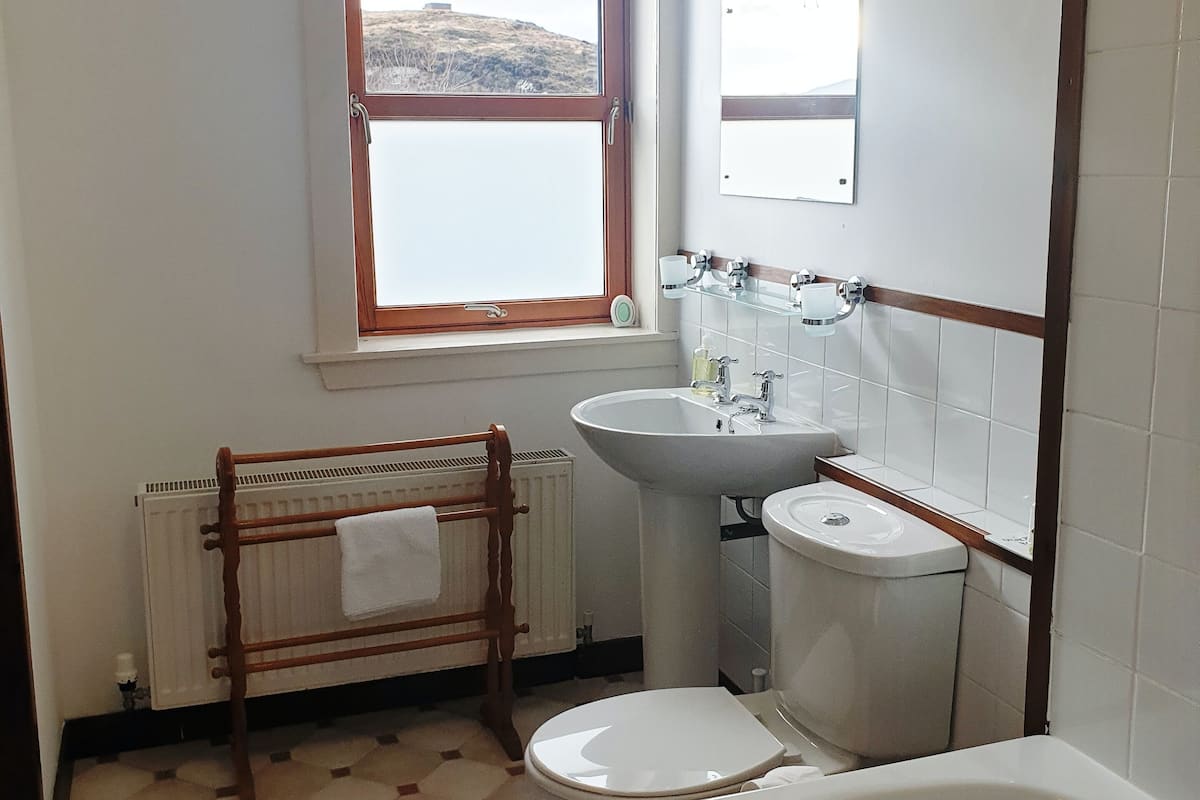 A bathroom with a window, a radiator, a sink, a toilet, and a bathtub.