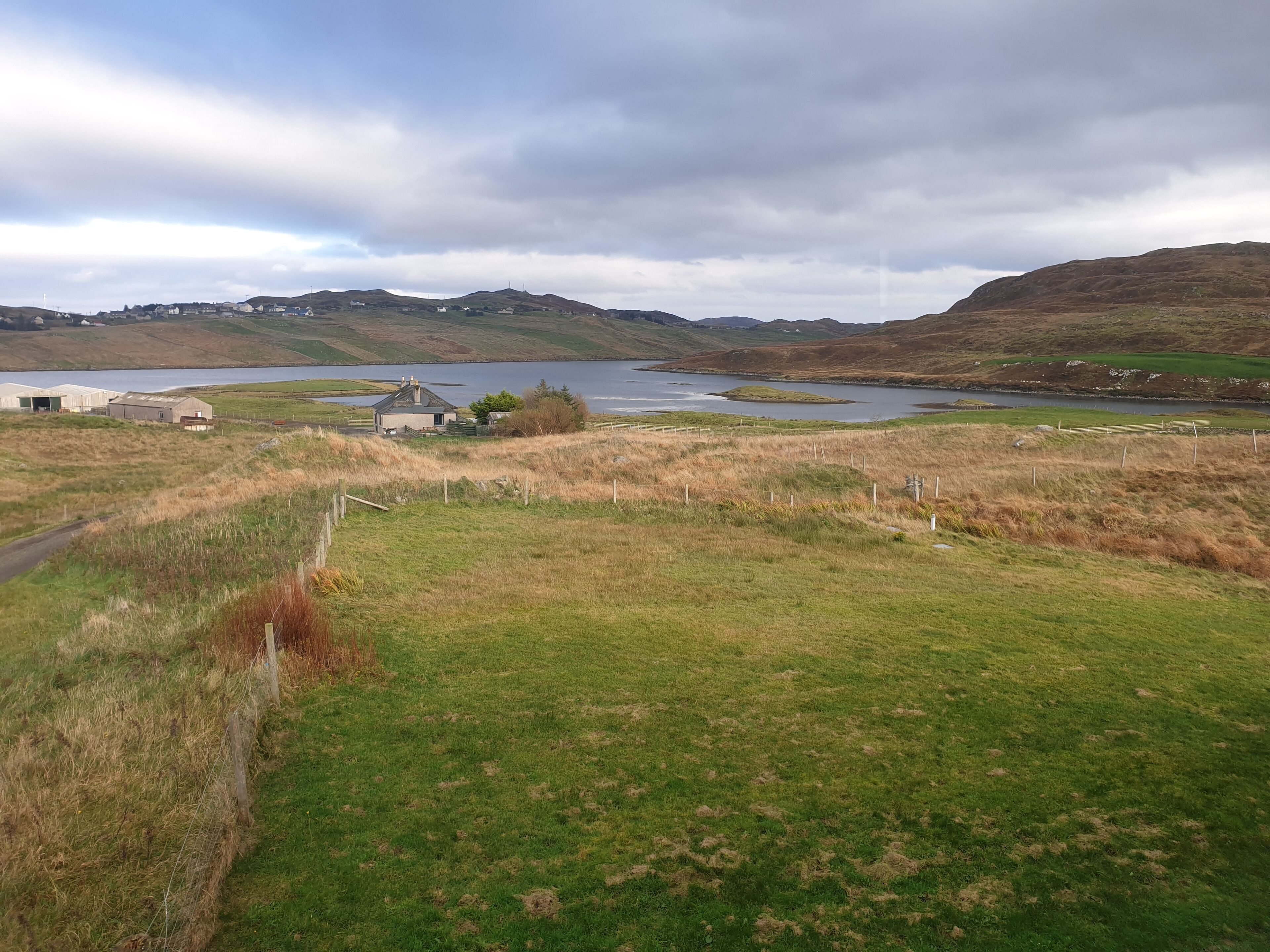 A rural landscape with a small house, a lake, and hills in the background.