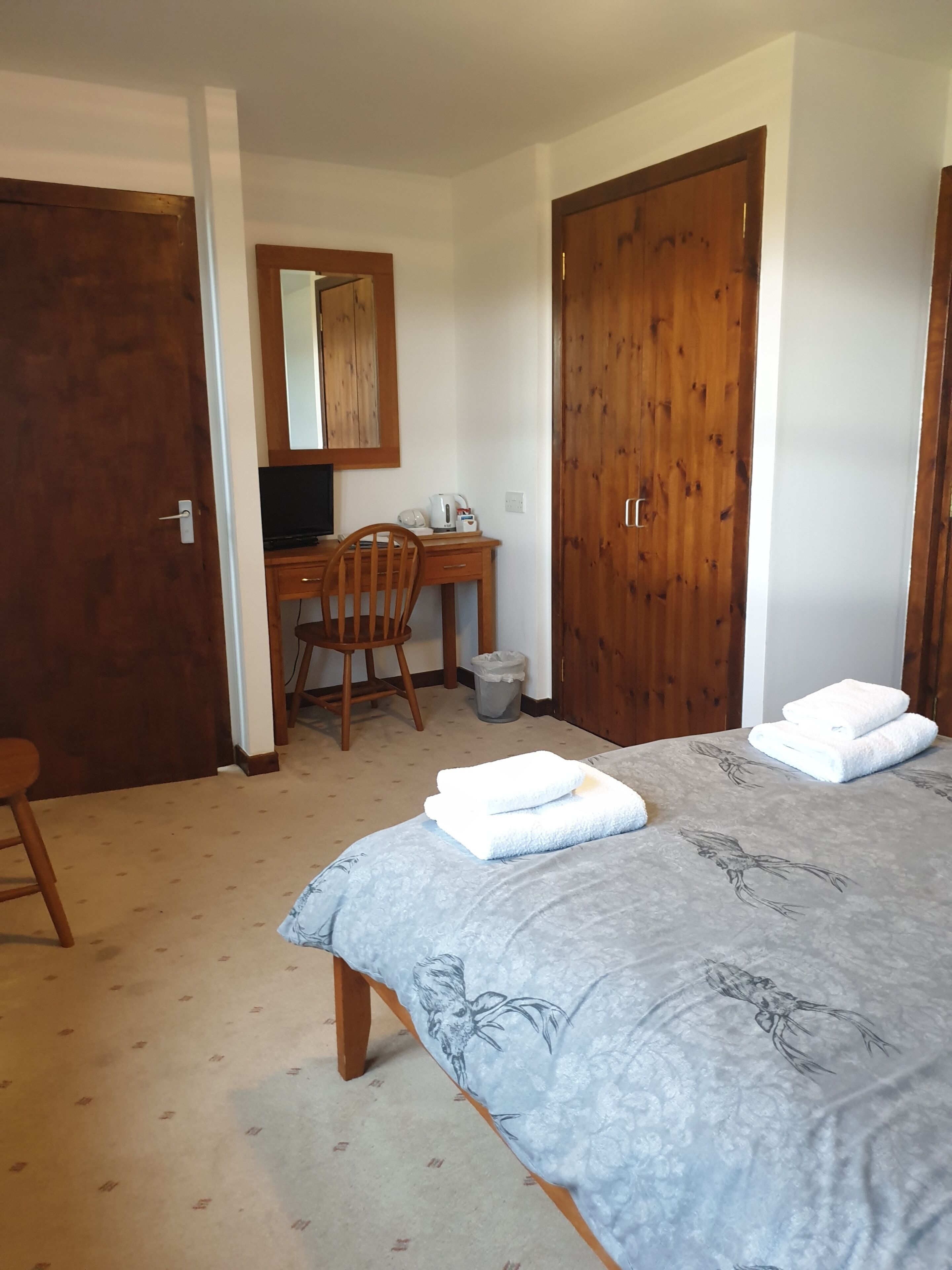 A bedroom with a bed, a desk, a chair, a mirror, and a wardrobe.