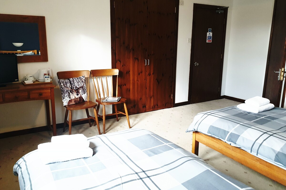 A hotel room with two beds, a desk with a computer, and two chairs.