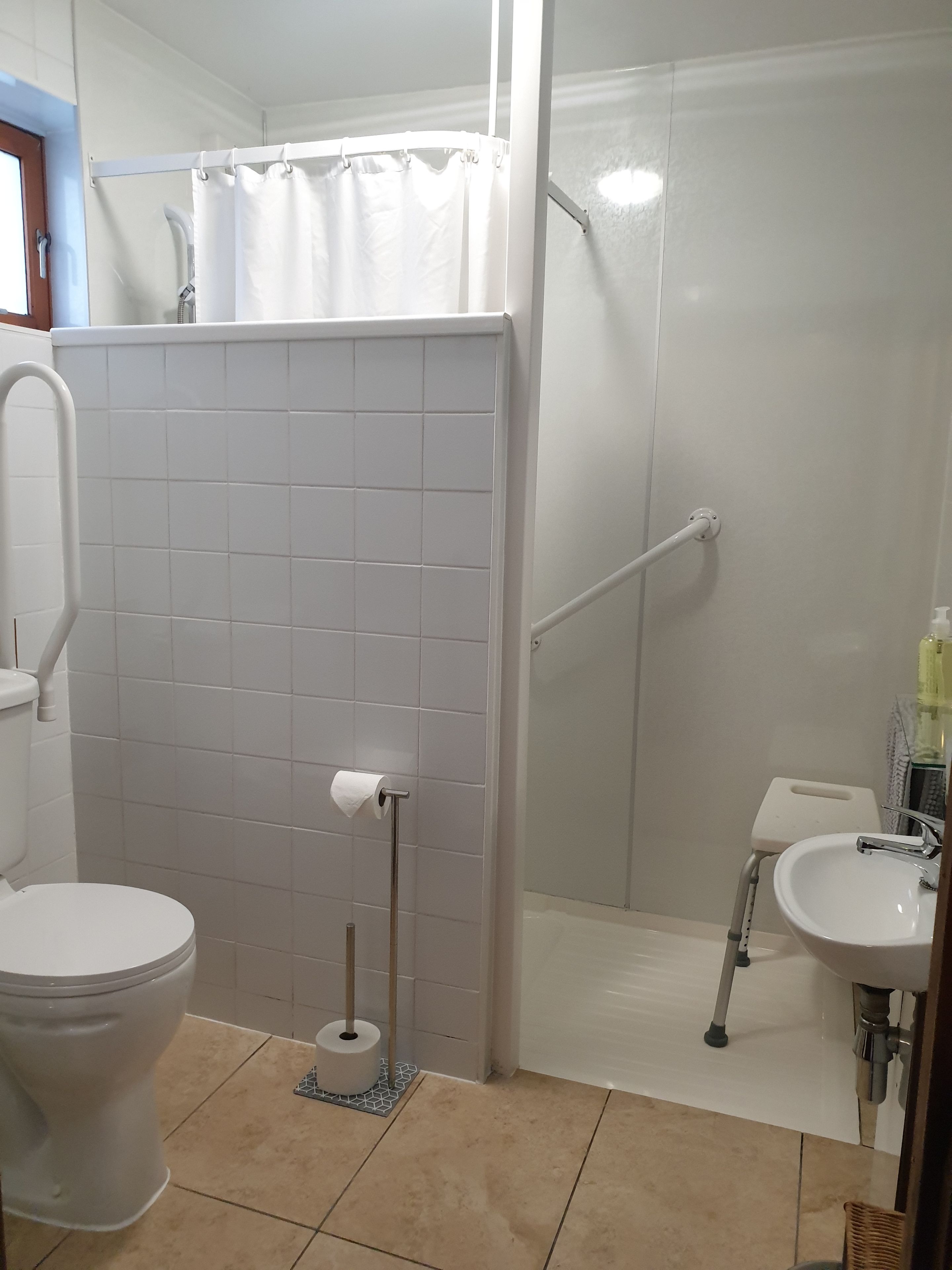 A bathroom with a toilet, a shower with a white curtain, a grab bar, and a sink with a mirror.